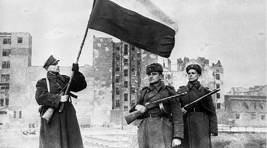 Советский и польский солдаты поднимают флаг в освобожденной...